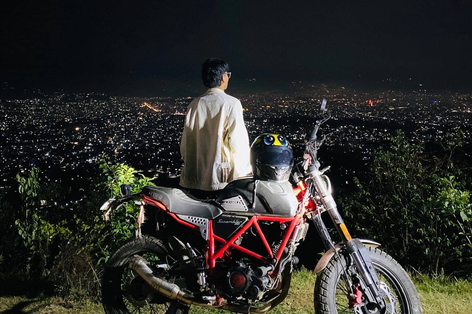 Raja Shahi on his scrambler motorcycle overlooking the night lights of Kathmandu from Whitehouse Resort