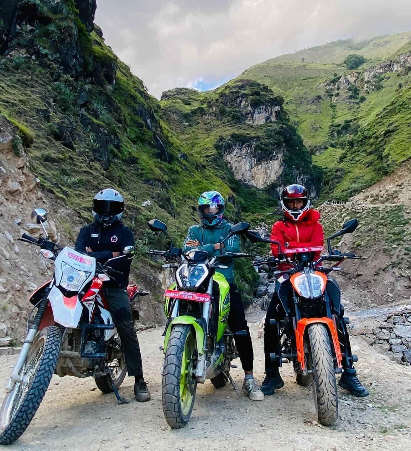 Three riders with motorcycles navigating a rugged mountain trail