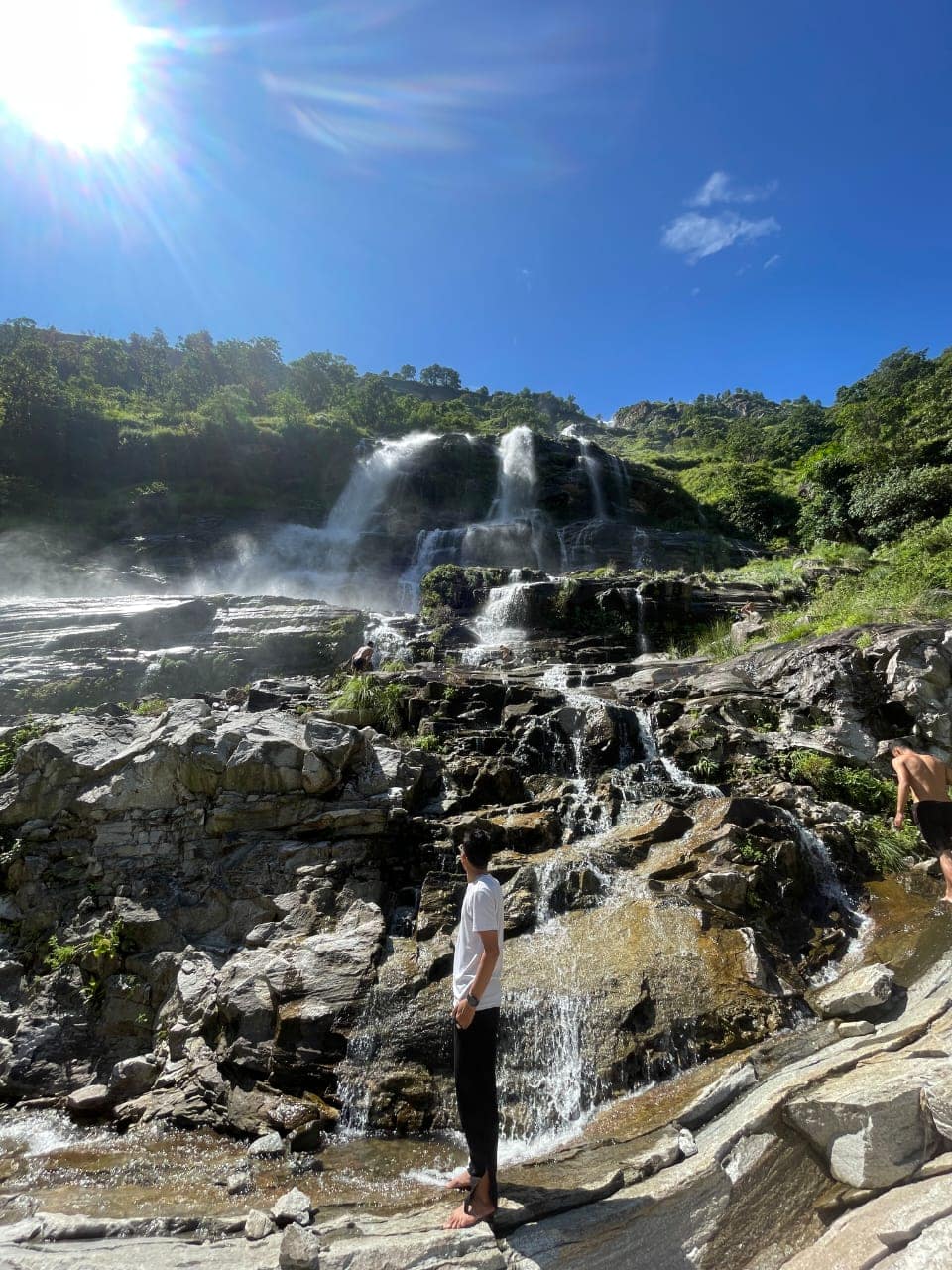 Cascading tiered mountain waterfall under bright sunny blue skies